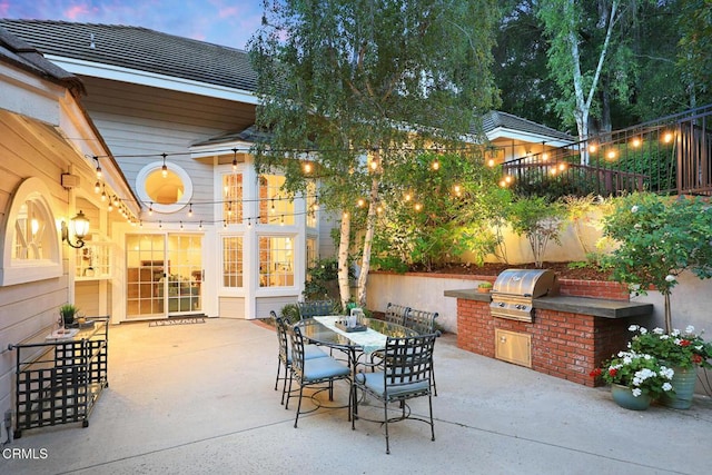 patio terrace at dusk with area for grilling, an outdoor kitchen, and outdoor dining space