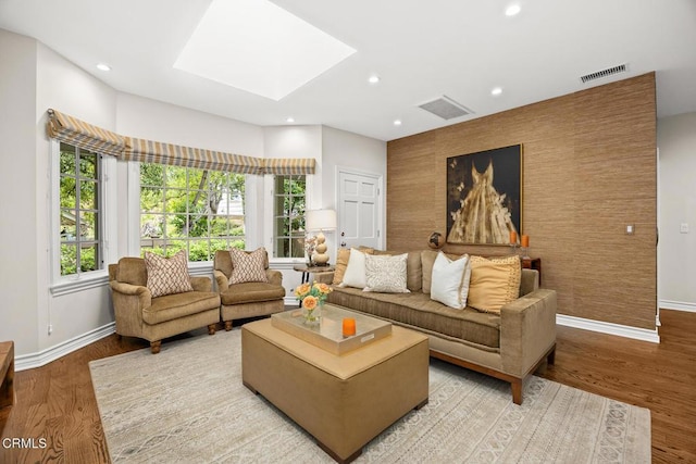 living area featuring an accent wall, baseboards, a skylight, recessed lighting, and light wood finished floors