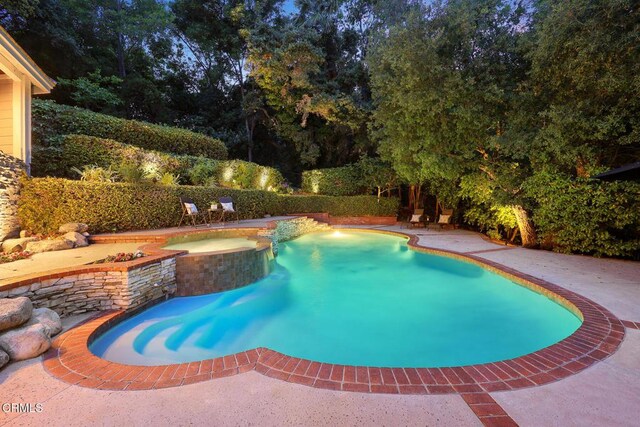 view of swimming pool with a pool with connected hot tub, a patio, and view of wooded area