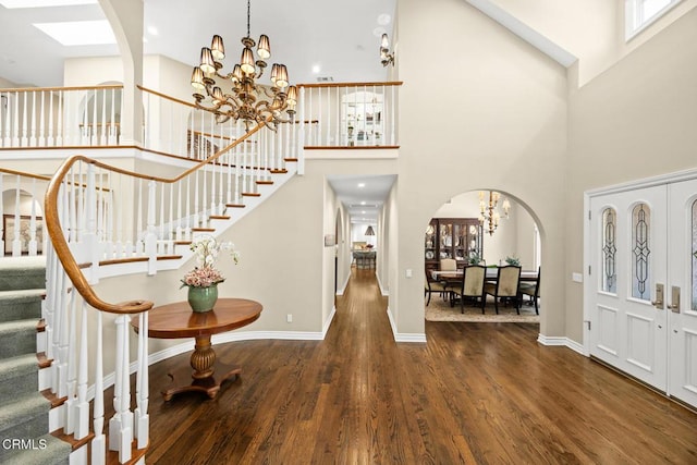 foyer entrance featuring a chandelier, arched walkways, stairs, wood finished floors, and high vaulted ceiling