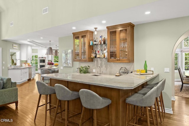 indoor wet bar featuring wood finished floors, decorative backsplash, recessed lighting, baseboards, and double oven