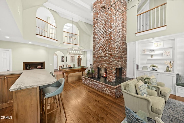 living room with a high ceiling, wood finished floors, arched walkways, a brick fireplace, and billiards