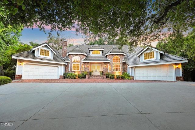 french country style house featuring a garage, a chimney, stone siding, and driveway