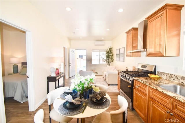 kitchen featuring stainless steel range with gas stovetop, wall chimney exhaust hood, an AC wall unit, wood finished floors, and a sink