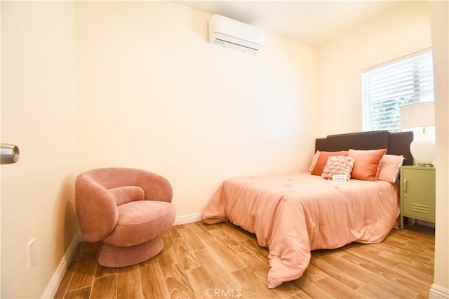 bedroom with an AC wall unit, light wood finished floors, and baseboards