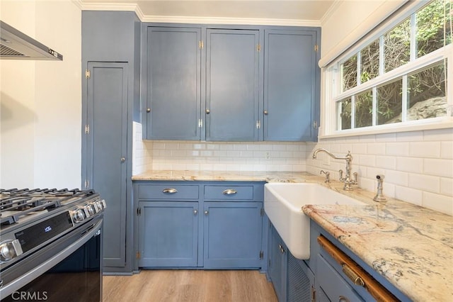 kitchen featuring stainless steel gas range, blue cabinets, wall chimney range hood, backsplash, and crown molding