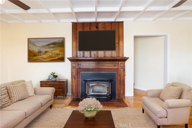 living area with coffered ceiling, a wood stove, light wood-style floors, beamed ceiling, and ceiling fan