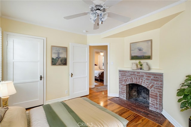 bedroom with wood finished floors, a fireplace, baseboards, ceiling fan, and crown molding