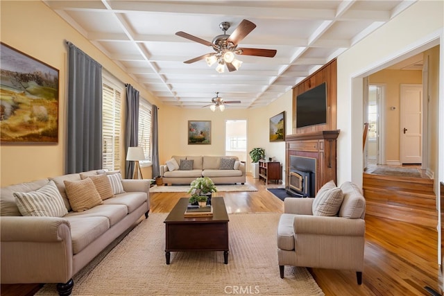 living area with coffered ceiling, wood finished floors, a ceiling fan, and beam ceiling