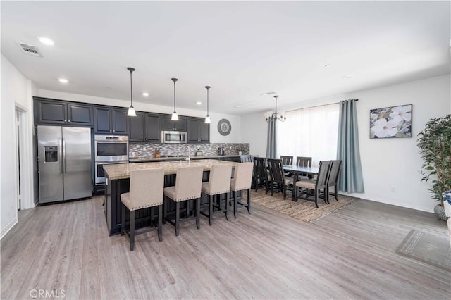 3225 E Denali Dr, Ontario, CA 91762 - kitchen with stainless steel appliances, a breakfast bar area, light wood-style floors, tasteful backsplash, and a center island with sink