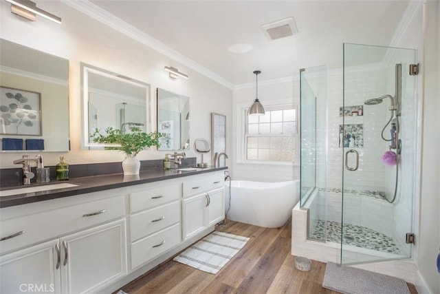 bathroom with a soaking tub, a shower stall, double vanity, wood finished floors, and ornamental molding