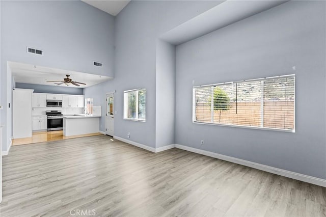 16129 Windcrest Dr, Fontana, CA 92337 - unfurnished living room with light wood-type flooring, healthy amount of natural light, ceiling fan, baseboards, and a high ceiling
