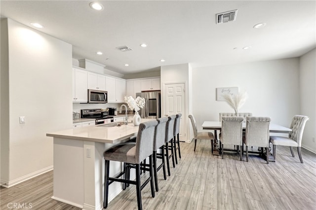 7354 Freesia Ln, Chino, CA 91708 - kitchen with appliances with stainless steel finishes, light wood-type flooring, a breakfast bar area, white cabinets, and baseboards