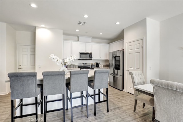7354 Freesia Ln, Chino, CA 91708 - kitchen with appliances with stainless steel finishes, a breakfast bar, white cabinetry, light wood-style flooring, and recessed lighting