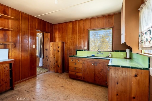 6425 Indian Cove Rd Unit 29, Palms, CA 92277 - kitchen with tile countertops, a sink, brown cabinetry, open shelves, and wood walls
