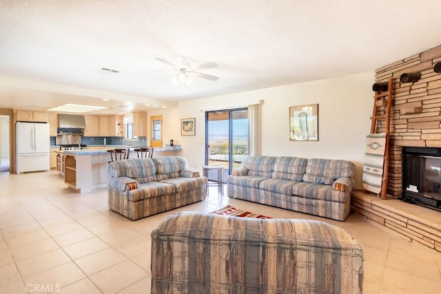 6425 Indian Cove Rd Unit 29, Palms, CA 92277 - living room featuring light tile patterned floors, ceiling fan, a stone fireplace, and a textured ceiling