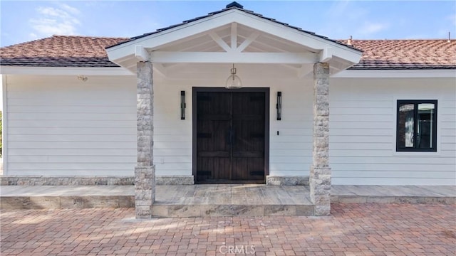 property entrance with an attached garage, a porch, and a shingled roof