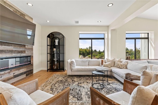 living area with wood finished floors, recessed lighting, arched walkways, a tiled fireplace, and baseboards