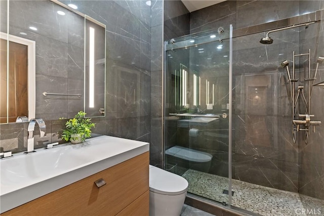full bath with toilet, a stall shower, vanity, tile walls, and tasteful backsplash