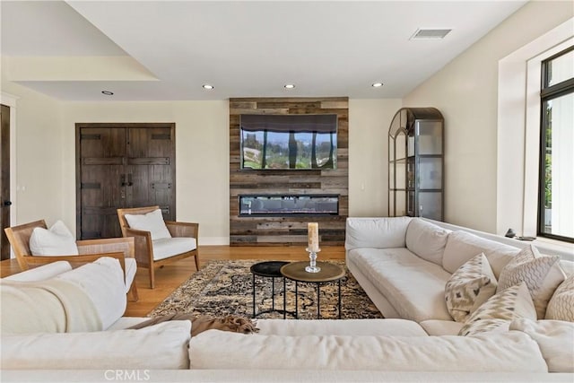 living room with a glass covered fireplace, wood finished floors, recessed lighting, and baseboards