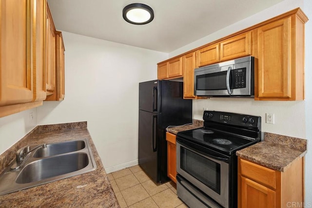 kitchen featuring appliances with stainless steel finishes, a sink, light tile patterned flooring, dark countertops, and baseboards