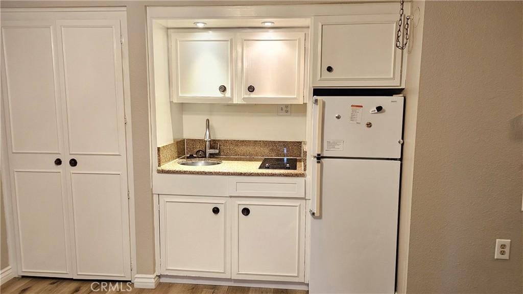 24055 Paseo Del Lago Unit 1153, Laguna Woods, CA 92637 - kitchen with freestanding refrigerator, a sink, white cabinets, light wood-type flooring, and stone countertops