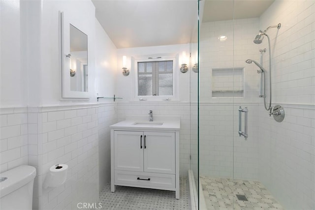 bathroom with a shower stall, tile walls, toilet, vanity, and a wainscoted wall