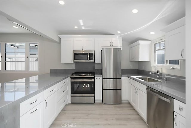 kitchen featuring stainless steel appliances, a sink, white cabinetry, recessed lighting, and vaulted ceiling