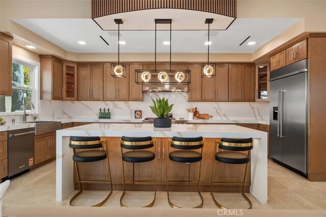 kitchen featuring stainless steel appliances, brown cabinetry, glass insert cabinets, a center island, and tasteful backsplash