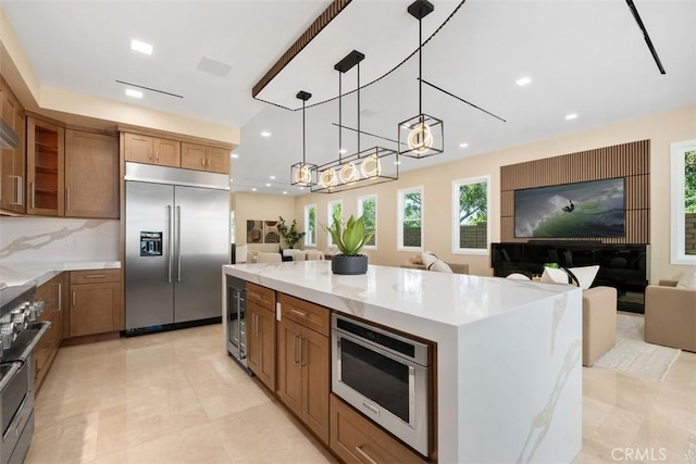 kitchen featuring built in appliances, open floor plan, beverage cooler, brown cabinetry, and hanging light fixtures
