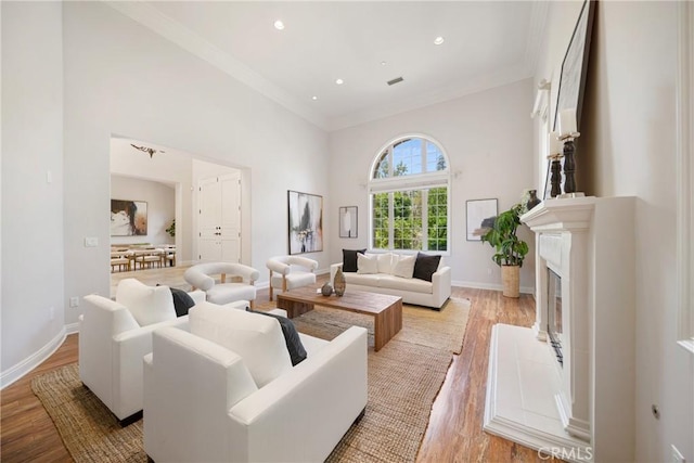 15850 Seville Ln, Encino, CA 91436 - living room featuring crown molding, light wood-style floors, a towering ceiling, baseboards, and a glass covered fireplace