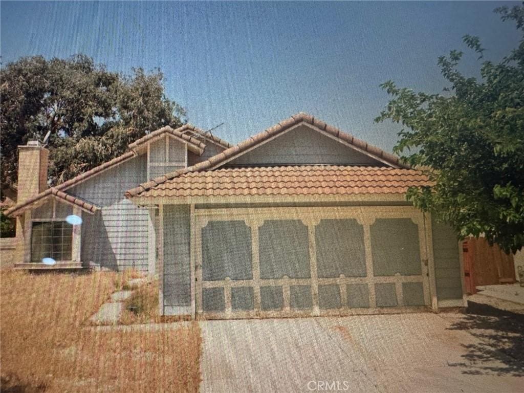 view of front of home with a garage, driveway, a tile roof, and a chimney