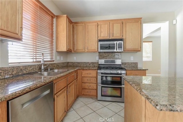 kitchen with stainless steel appliances, a sink, light tile patterned flooring, and dark stone counters