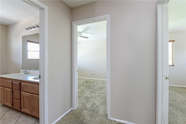 hall featuring light carpet, baseboards, and a sink
