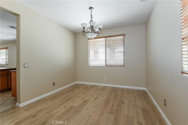 unfurnished room with light wood-style floors, a chandelier, and baseboards