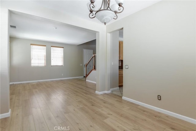 empty room featuring a chandelier, stairs, light wood-type flooring, and baseboards