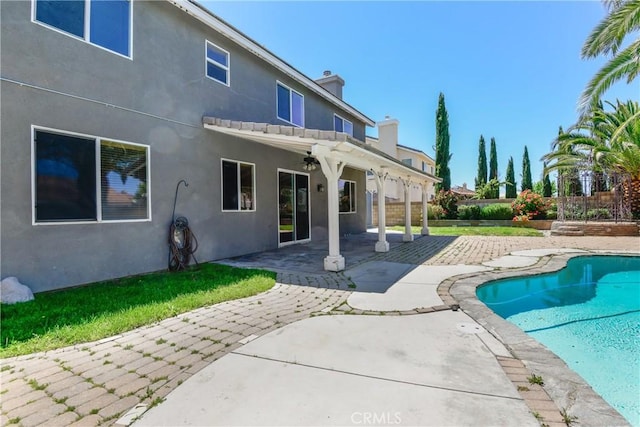 rear view of property with stucco siding, a patio, a chimney, a fenced backyard, and an outdoor pool