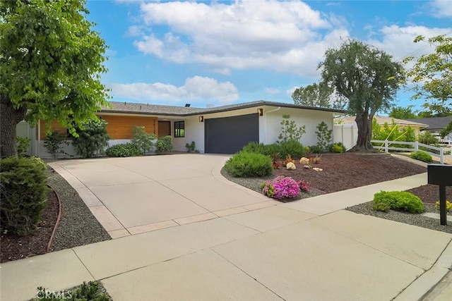 view of front of home featuring concrete driveway, an attached garage, fence, and stucco siding