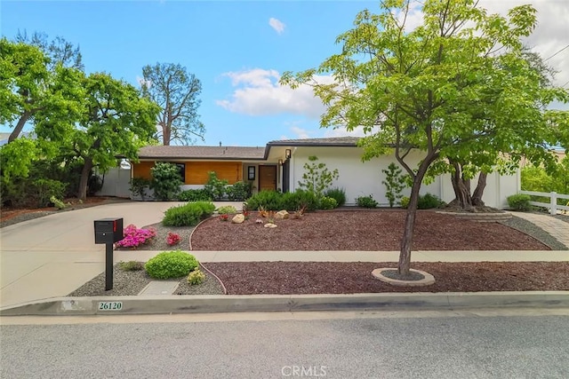 ranch-style house featuring curved driveway, fence, and stucco siding