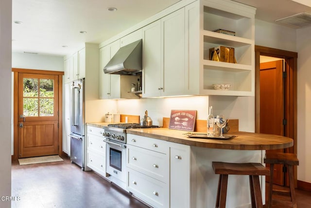 kitchen featuring wall chimney exhaust hood, appliances with stainless steel finishes, wooden counters, white cabinetry, and recessed lighting