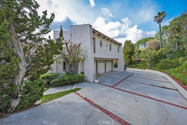 view of property exterior featuring stucco siding, an attached garage, concrete driveway, and a tile roof