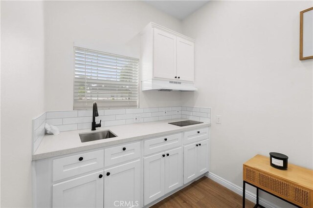 5927 Mckinley Ave, South Gate, CA 90280 - kitchen with under cabinet range hood, a sink, light countertops, black electric cooktop, and white cabinets