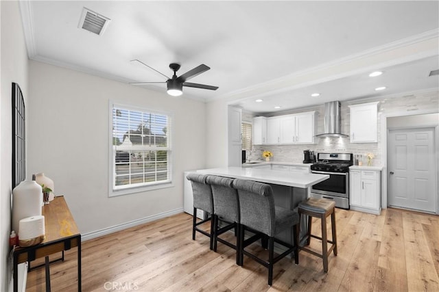 5927 Mckinley Ave, South Gate, CA 90280 - kitchen with stainless steel gas range, wall chimney exhaust hood, light countertops, white cabinetry, and a kitchen bar