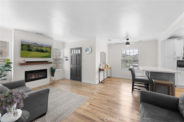5927 Mckinley Ave, South Gate, CA 90280 - living area featuring a glass covered fireplace, light wood-style floors, ornamental molding, a ceiling fan, and baseboards