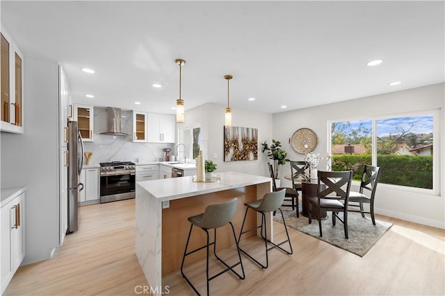 27751 Via Lorca, Mission Viejo, CA 92692 - kitchen with wall chimney range hood, stainless steel appliances, light wood-style floors, a kitchen breakfast bar, and glass insert cabinets