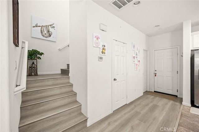 foyer entrance featuring light wood-type flooring, stairway, and baseboards
