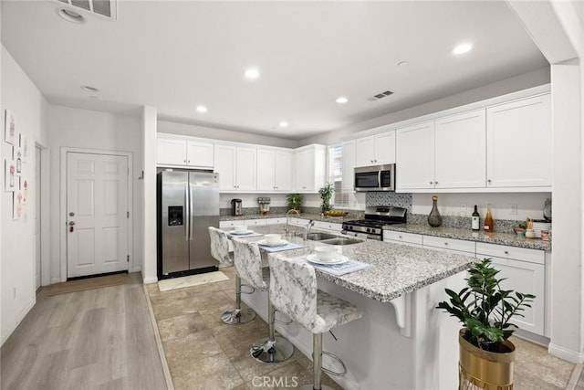 kitchen with stainless steel appliances, a sink, white cabinets, an island with sink, and a kitchen bar