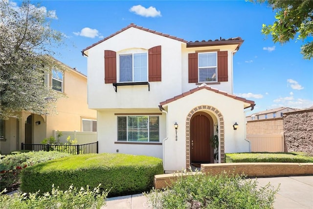 mediterranean / spanish-style home featuring a tiled roof, stucco siding, and fence