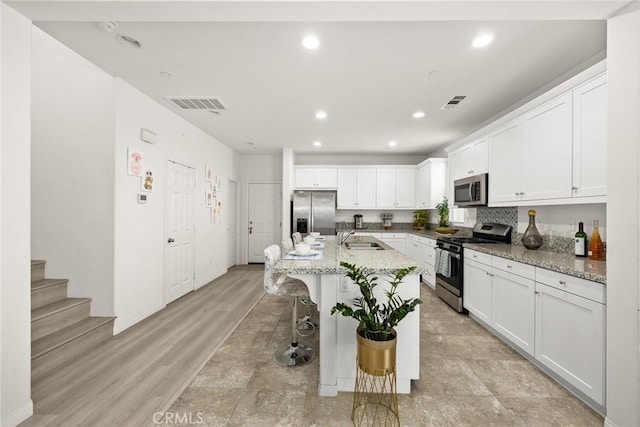 kitchen with stainless steel appliances, a sink, a kitchen bar, white cabinets, and a kitchen island with sink