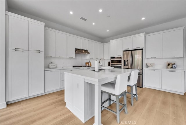 107 Plum Lily, Irvine, CA 92618 - kitchen with stainless steel fridge, under cabinet range hood, a kitchen island with sink, light wood-style floors, and recessed lighting